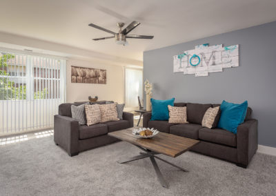 Living room with carpet flooring, grey couches, coffee table, and large windows