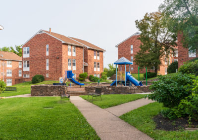 Creekside Apartments exterior with red brick buildings and a blue jungle gym