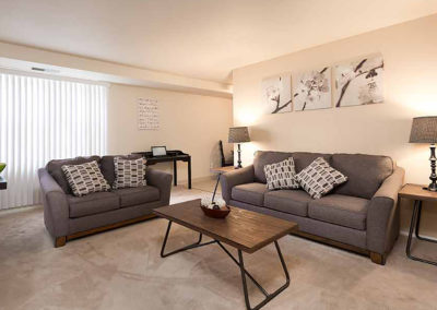 Living room with carpet flooring, grey couches, coffee table, and large windows